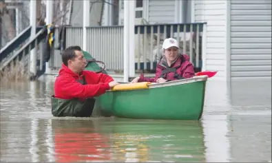  ?? Canadian Press photo ?? Julie Theriault (right) and Jean-Francois Perrault push a canoe with neighbour's belongings as they help in the flooded area of Gatineau, Que. Sunday.