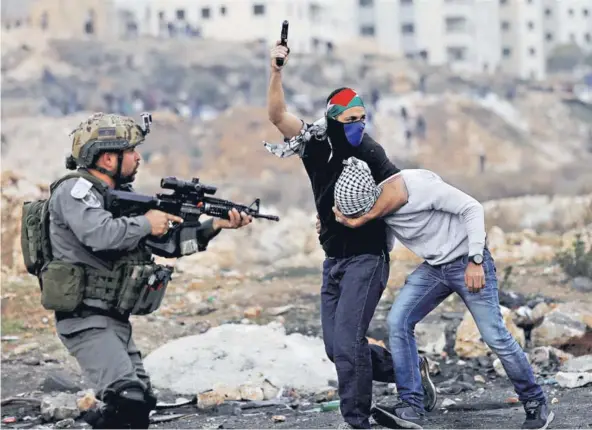  ??  ?? ► Un agente de las fuerzas de seguridad israelí con la bandera palestina en la frente detiene a un palestino cerca de Ramala, ayer.