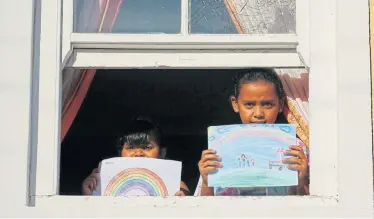  ?? Picture: SUMAYA HISHAM/REUTERS ?? LONG BREAK: Bashierah Moos, 5, left, and Hanaa Moos, 9, hold up pictures they drew during lockdown, as they stand by a window at their house in Cape Town this week. Bashierah said: ‘I feel sad because I can’t see my friends and go to school’