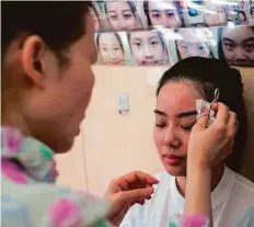  ?? AFP ?? A customer has her eyebrows plucked by trained face reader Li Chau-jing.