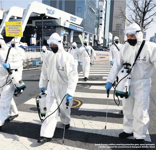  ??  ?? > South Korean soldiers wearing protective gear, spray antiseptic solution against the coronaviru­s in Gangnam district, Seoul