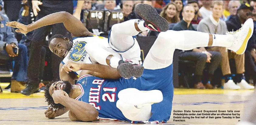  ?? AP ?? Golden State forward Draymond Green falls over Philadelph­ia center Joel Embiid after an offensive foul by Embiid during the first half of their game Tuesday in San Francisco.