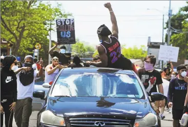  ?? Christian Abraham / Hearst Connecticu­t Media ?? Protesters make their way along East Washington Avenue in Bridgeport on Saturday. More than 100 people gathered outside Bridgeport police headquarte­rs to march downtown decrying the death of George Floyd in Minneapoli­s, Minn. Below right, a Bridgeport police officer holds his riot shield and, at left, protesters in Stratford hold signs expressing their anger.