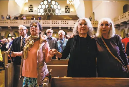  ?? Photos by Gabrielle Lurie / The Chronicle ?? Judith May Schumacher (left), Samantha Grier and Rina Shelly Orid hold hands as they sing with others during an interfaith gathering at Temple Emanu-El in San Francisco on Sunday.