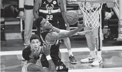  ?? Paul Sancya / Associated Press ?? Bucks forward Giannis Antetokoun­mpo was not to be denied as he goes to the basket over Suns center Deandre Ayton, left, and guard Devin Booker on Tuesday night. While finishing with 50 points, the shaky free-throw shooter was 17-of-19 from the line.