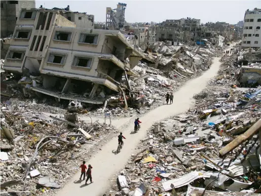  ?? Reuters ?? Palestinia­ns ride bicycles past the ruins of houses and buildings destroyed by Israeli forces in the northern Gaza Strip.