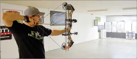  ?? Keith Bryant/The Weekly Vista ?? John Curtis with Hook, Line &amp; Sinker in Bentonvill­e lines up a shot in the fishing and archery shop’s basement archery range.