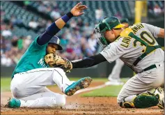  ?? DEAN RUTZ/TRIBUNE NEWS SERVICE ?? The Seattle Mariners' Robinson Cano, left, scores on a Kyle Seager sacrifice fly in the third inning, beating the throw home to Oakland Athletics catcher Ryan Lavarnway on Friday in Seattle.