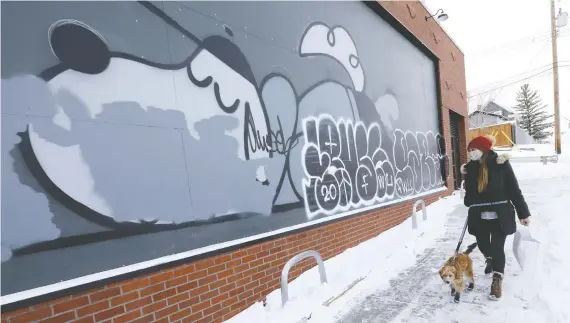  ?? PHOTOS: DARREN MAKOWICHUK ?? Sandra Chung walks her dog, Hawlow, past graffiti on the side of a building under constructi­on in Bridgeland that will house a number of food businesses.