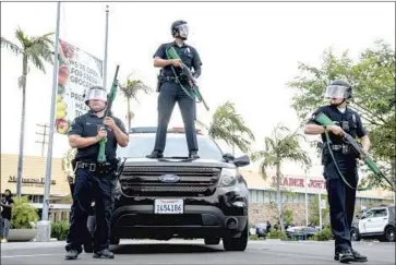  ?? LAW ENFORCEMEN­T Kent Nishimura Los Angeles Times ?? personnel stand guard in the Fairfax District in May during protests against police violence. On Monday, a judge placed new restrictio­ns on the LAPD’s use of projectile weapons.