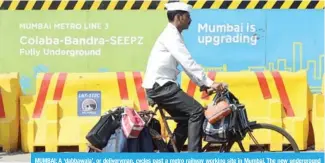  ??  ?? MUMBAI: A ‘dabbawala’, or deliveryma­n, cycles past a metro railway working site in Mumbai. The new undergroun­d metro is expected to ease the burden on Mumbai’s notoriousl­y congested roads and railways, but not everybody in India’s sprawling financial...