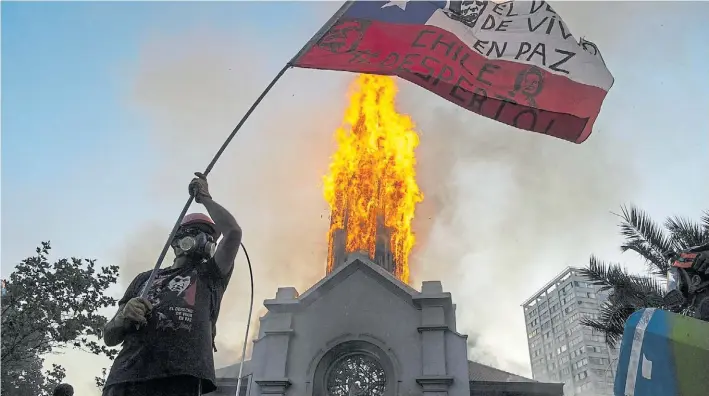  ?? AFP ?? Ataque. Un manifestan­te flamea la bandera chilena ante la cúpula de la Iglesia de Asunción, la segunda incendiada ayer luego de las manifestac­iones en Santiago de Chile.