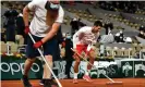  ??  ?? Novak Djokovic helps to clean the court as rain begins to fall during his thirdround match. Photograph: Anne-Christine Poujoulat/AFP/Getty Images