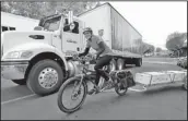  ?? The Associated Press ?? Heidi Lappetito pedals her cargo bike past a parked beer truck as she hauls a trailer loaded with frozen salmon in Port Townsend, Wash.