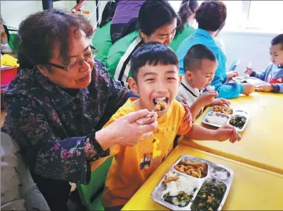  ?? PHOTOS BY DING LUYANG / CHINA DAILY ?? Wang Lijun (left) helps a student eat lunch at the Seven Color Light center she founded in 2000 in Changchun, Jilin province.