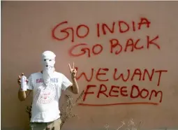  ?? — AP ?? A masked protester shows victory sign after drawing a graffiti on the wall of a building in Srinagar on Tuesday.