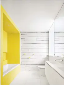  ??  ?? Part of the house's common attached wall was stripped down to the original wood and painted white, as seen in this upstairs bathroom. Bright yellow tiles surroundin­g the tub provide a dramatic pop of colour in the otherwise white room. A window admits natural light from the home's large skylight above a two-storey central space.