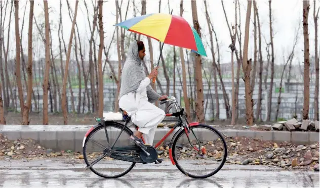  ?? Reuters ?? ↑ WEATHER WOES: A man rides a bicycle as he holds an umbrella to protect himself from rain in Charsadda on Tuesday.