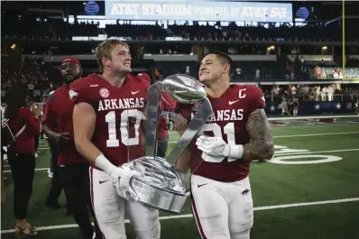  ?? NWA Democrat-Gazette/Charlie Kaijo ?? ■ Arkansas linebacker­s Bumper Pool (10) and Grant Morgan (31) carry the Southwest Classic trophy at the end of a Sept. 25 football game at AT&T Stadium in Arlington, Texas. The Razorbacks will face the Penn State Nittany Lions at 11 a.m. in the Outback Bowl at Raymond James Stadium in Tampa, Fla.