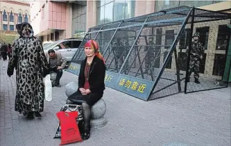  ?? NG HAN GUAN THE ASSOCIATED PRESS ?? A Uighur woman rests near a cage protecting heavily armed Chinese paramilita­ry officers on duty in Urumqi in China’s northweste­rn region of Xinjiang in 2014.