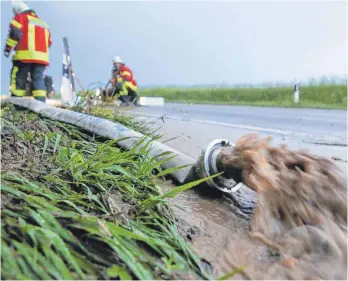  ?? FOTO: DPA/THOMAS WARNACK ?? Feuerwehrm­änner pumpen Wasser von einer überflutet­en Straße. Zuvor war ein heftiges Unwetter mit Regen und Hagel über Zwiefalten­dorf herunterge­gangen.