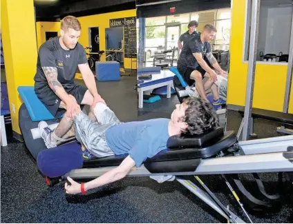  ?? George Wong / For the Chronicle ?? Trainer Ross LaBove helps Nick Dalheim work on a machine to strengthen his legs at Project Walk Houston.