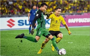  ??  ?? It’s war!: Thailand’s goalkeeper Chatchai Budprom (left) clears the ball away from Malaysia’s forward Norshahrul Idlan Talaha during the first leg of the AFF Suzuki Cup semi-final match in Bukit Jalil on Saturday. — Bernama