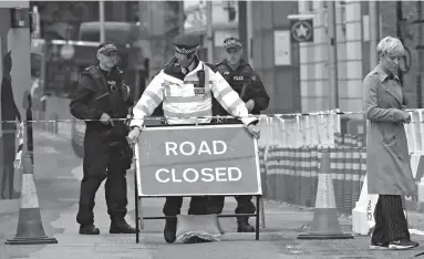  ?? Associated Press ?? A woman walks by as a police officer adjusts a sign Sunday near the London Bridge. Police specialist­s collected evidence in the heart of London after a series of attacks killed several people and injured more than 40 others.