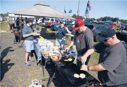  ?? JESSICA HILL PHOTOS/SPECIAL TO THE COURANT ?? Dan Kish of Brookfield, right, and friend Carl Abrahamson, second from right, of New York, cook for friends as they tailgate before UConn’s football game against Holy Cross on Saturday at Rentschler Field. The Huskies lost 38-28.