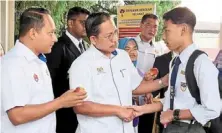  ?? ?? Welcome back!: azman (centre) and aznan (left) greeting and handing out apples to students on the first day of school at SMK Sultan Ismail, Johor Baru.