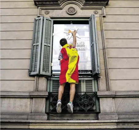  ?? BILD: SN/AP ?? Ein Demonstran­t klebt einen Spanien-Sticker an die Auslage einer Bank in Barcelona.