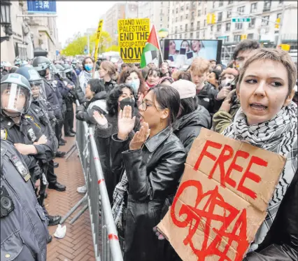  ?? Mary Altaffer The Associated Press ?? Police in riot gear stand guard as demonstrat­ors chant slogans outside the Columbia University campus in New York last month.