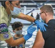  ?? Irfan Khan Los Angeles Times ?? ORION PATRON, 5, watches as Reserve Deputy Adrienne Brod administer­s a COVID-19 shot to his father, Deputy Ronald Patron, at a site in Pomona.