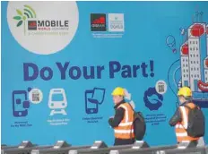  ?? — Reuters ?? Workers walk past a banner of the Mobile World Congress in Barcelona.