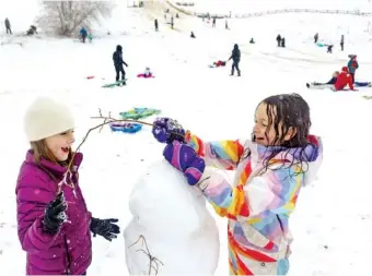  ?? SARAH A. MILLER/IDAHO STATESMAN VIA AP ?? Above: Friends Addie Palmer, 7, left, and Esther Roghaar, 7, right, use tree branches to make arms and even hair on a snowman Monday at Camel’s Back Park in Boise, Idaho. The National Weather Service reported 2.5 inches of snow accumulati­on overnight from their location at the Boise Airport. No more snow is in the forecast for the Boise area this week, but temperatur­es are expected to drop to as low as 6 degrees by Saturday night.