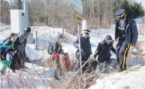  ??  ?? Mounties help a family of asylum-seekers as they cross the U.S.-Canada border this week south of Hemmingfor­d, Que.
