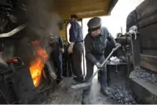  ??  ?? A worker shovels coal into a locomotive’s steam engine.