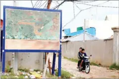  ?? HENG CHIIVOAN ?? Two men ride past a map of the proposed extension of Phnom Penh Internatio­nal Airport earlier this week.