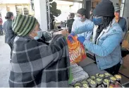  ?? Andy Cross, The Denver Post ?? Volunteer Donavan Allen, right, helps customer Juana Cruz load up her bag Wednesday at Emerald Garden’s East Denver Food Hub at the Lost City Market.