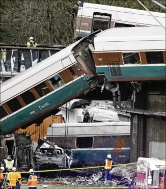  ?? ELAINE THOMPSON / ASSOCIATED PRESS ?? Amtrak train cars dangle from tracks near smashed vehicles on Interstate 5 after a derailment Monday in DuPont, Wash. An official briefed on the investigat­ion said early signs indicate that Train 501 may have struck something before going off the track...