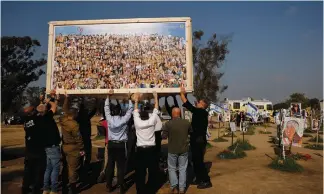  ?? (Susana Vera/Reuters) ?? PEOPLE HELP raise a collage by artist Amir Chodorov last week, depicting the faces of the Supernova music party victims in Kibbutz Re’im.