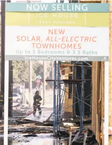  ??  ?? A firefighte­r works near an ad for the new townhomes, part of a complex of buildings destroyed by the fire.