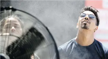  ??  ?? Xavier Selly cools down in front of a large fan equipped with a water misting ring at the Montreal jazz fest on Tuesday. ALLEN McINNIS / POSTMEDIA NEWS