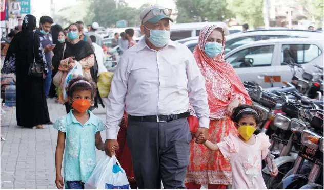  ?? Associated Press ?? ↑
A family, wearing face masks, shops at a market in Karachi on Wednesday.