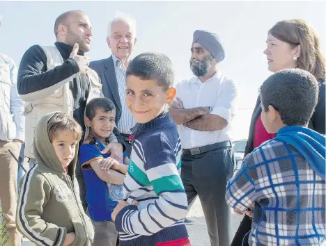  ?? PAUL CHIASSON/THE CANADIAN PRESS ?? Young Syrian refugees gather around Minister of Immigratio­n, Refugees and Citizenshi­p John McCallum, second from left, Defence Minister Harjit Sajjan and Health Minister Jane Philpott, right, as they tour the Zaatari Refugee Camp, near the city of...