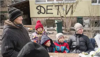  ?? ?? People wait for a free food delivery in Bucha on the outskirts of Kyiv, Ukraine. The graffiti written by the neighbors on the wall in background reads “Children.”