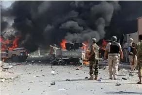  ?? AFP / Getty Images ?? Fighters from the forces loyal to Libya’s Government of National Unity stand near burning vehicles after an Islamic State suicide bomb attack.