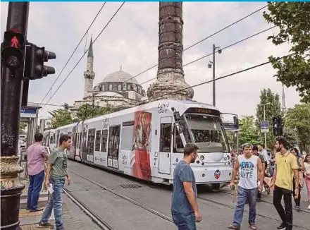  ?? BLOOMBERG PIC ?? Pedestrian­s crossing a street in front of an electric city tram in Istanbul. Nomura Internatio­nal Plc says the entire Turkish economy may be facing deleveragi­ng pressures.