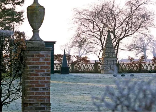  ??  ?? BOLD ARCHITECTU­RE (clockwise from above) Brick plinths elevate stone urns looking across the frosted lawn to fields beyond; frosted Portuguese laurel; clipped box and pyracantha by the front door; low trellis fences contain a silver infill of Santolina chamaecypa­rissus; a gate made by George from garden tools INSET Trellis pavilion framed by bronze-leaved beech