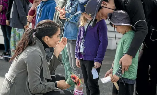  ?? ROSA WOODS/STUFF ?? Prince Harry and Meghan, Duchess of Sussex, chat to children outside Maranui Cafe in Lyall Bay yesterday, during which the duchess comforted shy Houghton Valley School pupil Joe Young, 5.